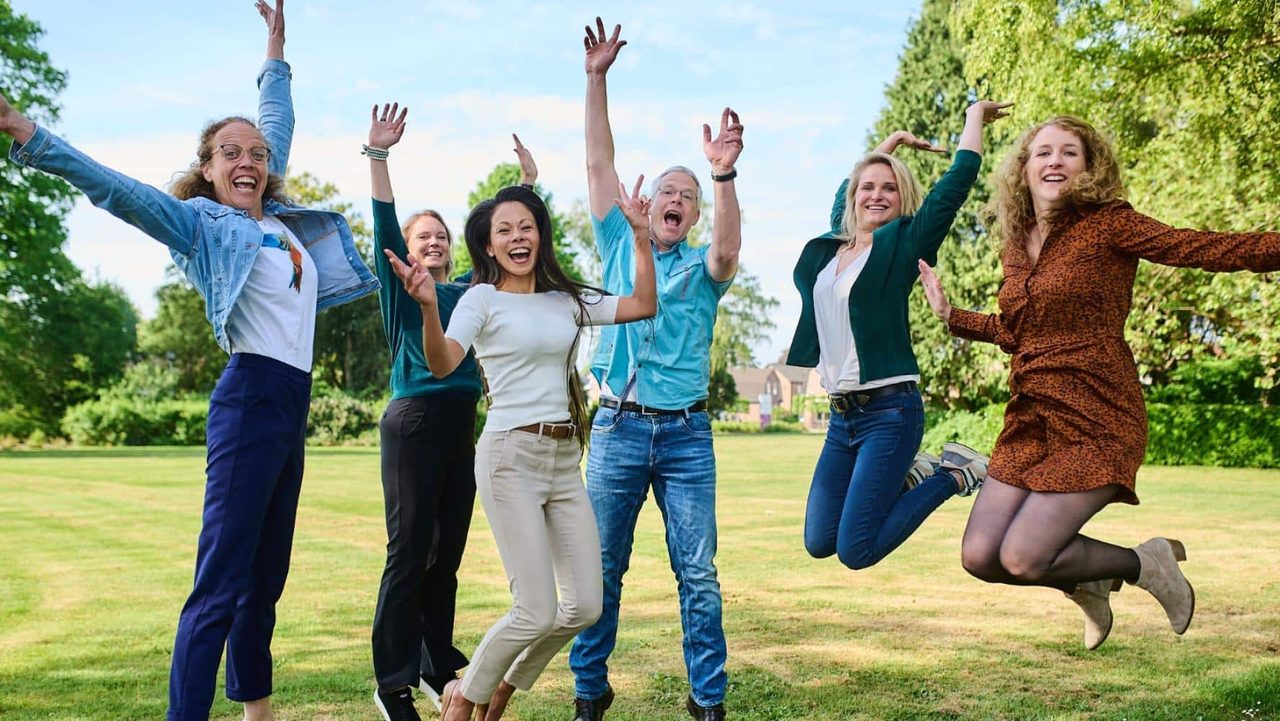 Zes mensen springen juichend op een grasveld