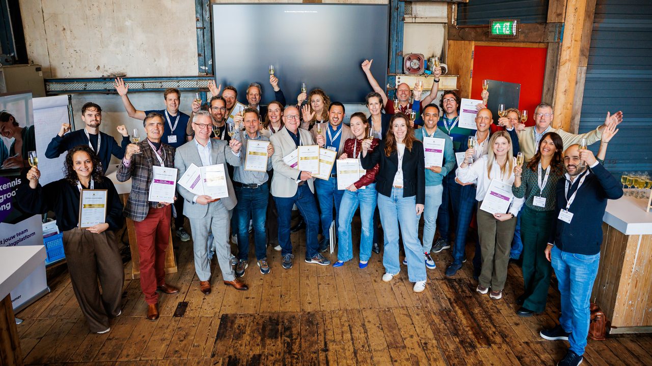 Groep deelnemers met certificaten en een glas in de hand tijdens de uitreiking van de e-Academy-certificering aan scholen